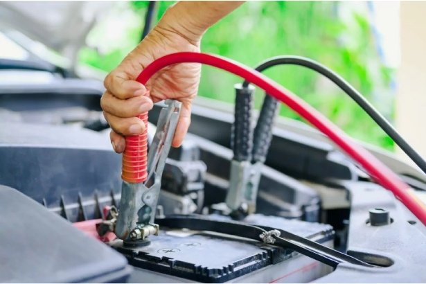 Hand connecting heavy-duty battery jumper cables for emergency car start.