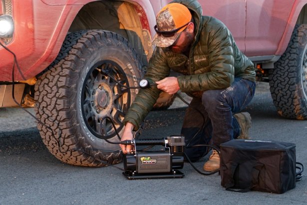 Portable tire inflator in use by off-road driver, essential mechanical tool for 4x4 recovery.