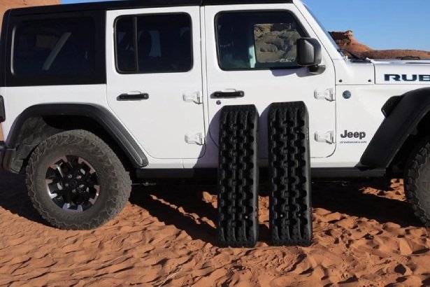 Pair of traction boards placed beside a Jeep for off-road recovery in sandy terrain.
