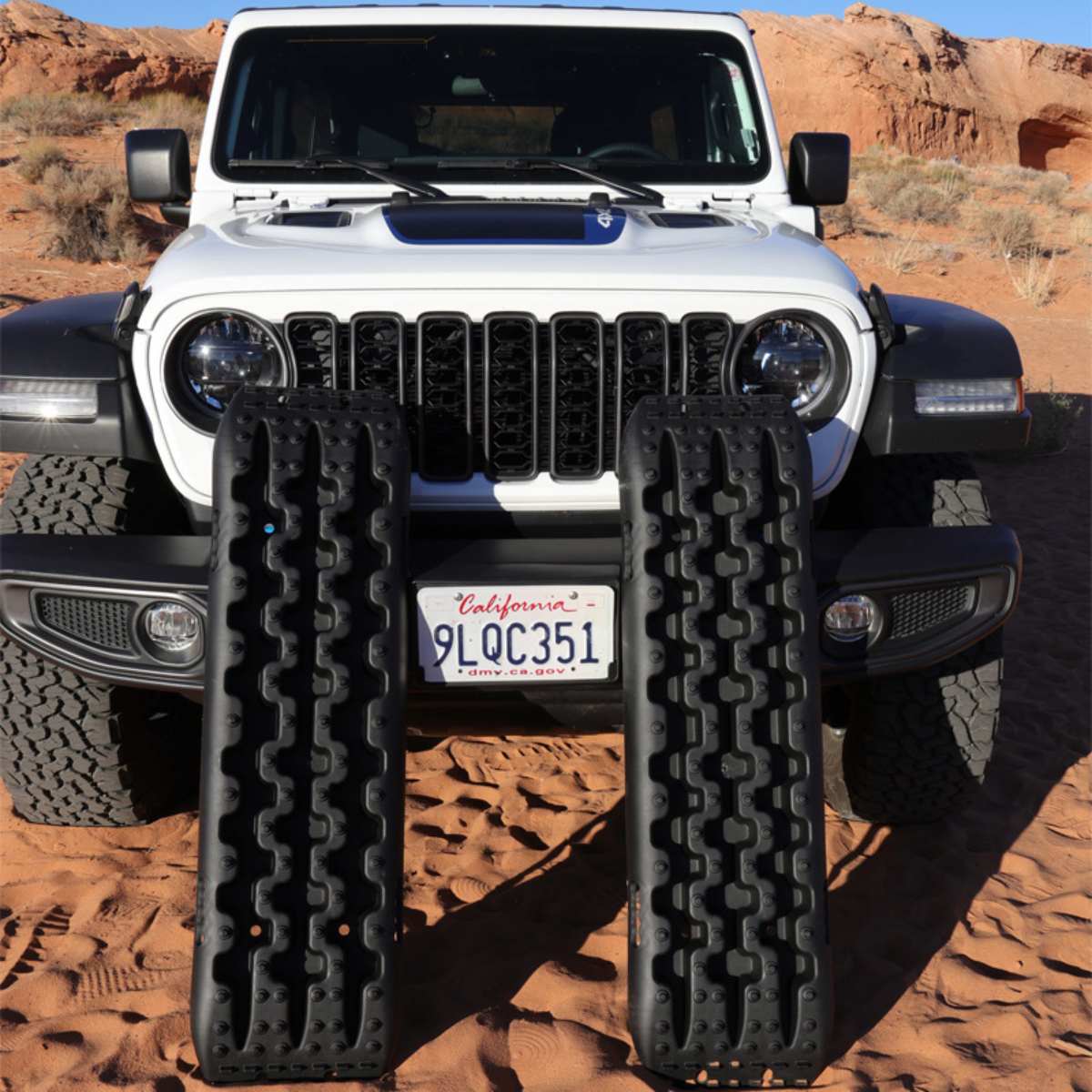 Black traction boards placed in front of a Jeep on desert terrain